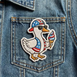 May include: Embroidered patch featuring a cartoon goose wearing sunglasses and a patriotic hat, holding an ice cream cone. The goose has a red, white, and blue design, and is set against a denim jacket pocket.