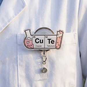 May include: A badge reel featuring a periodic table design with the chemical symbols Cu for Copper and Te for Tellurium, spelling out the word CuTe. The design includes illustrations of a pink liquid-filled flask and a test tube with hearts.