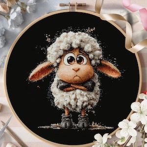 May include: Cross-stitch embroidery of a sheep with a fluffy white wool coat, large brown eyes, and crossed arms. The sheep is set against a black background within a wooden embroidery hoop. Decorative flowers and ribbons surround the hoop.