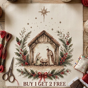 May include: A cross-stitch fabric piece featuring a nativity scene inside a wooden stable, surrounded by a wreath of green holly leaves and red berries. A star shines above the stable. The text "BUY 1 GET 2 FREE" is printed at the bottom.