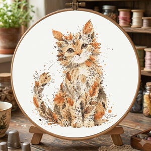 Op de afbeelding: Een ronde houten borduurring met een kruissteekpatroon van een kat. De kat is weergegeven in tinten oranje, bruin en wit, met een textuur die wordt gecreëerd door individuele steken op een witte ondergrond van stof.