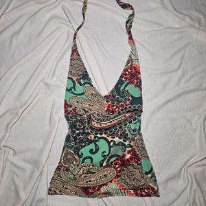 May include: A halter-neck top featuring a vibrant paisley pattern in shades of mint green, deep red, black, and cream. The garment has a deep V-neckline, a fitted bodice, and thin straps that tie behind the neck, showcasing a complex, swirling design.