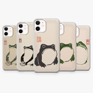 May include: A collection of five phone cases featuring frog illustrations in various colors. Each case has a beige background and a different frog design, including black, green, and a frog with a bowl. The cases have a clear, protective design.