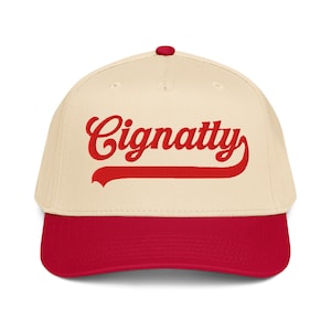 Könnte beinhalten: Baseballcap mit cremefarbener Krone und rotem Schirm. Das Wort "Cignatty" ist in roter Schrift auf der Vorderseite gestickt.