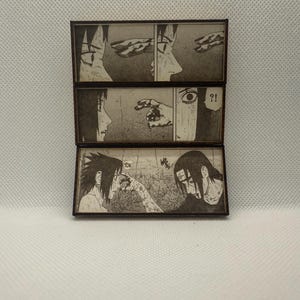 Peut inclure: Pr&eacute;sentoir en bois &agrave; trois niveaux avec des panneaux illustr&eacute;s en noir et blanc de manga. Les panneaux repr&eacute;sentent des sc&egrave;nes avec des personnages dans un r&eacute;cit dramatique, avec des bulles et des lignes d'action.