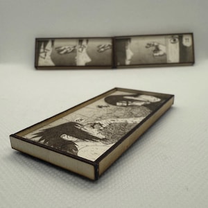 Peut inclure: Pi&egrave;ces d'art rectangulaires en bois avec des illustrations de manga en noir et blanc. L'&oelig;uvre est encadr&eacute;e d'une bordure marron clair. Une pi&egrave;ce est mise au point, tandis qu'une autre est en arri&egrave;re-plan. Les panneaux de manga repr&eacute;sentent une sc&egrave;ne dramatique.
