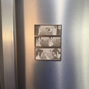 Peut inclure: Trois aimants rectangulaires &agrave; cadres noirs, chacun affichant un panneau diff&eacute;rent d'un manga. Les panneaux sont en noir et blanc et repr&eacute;sentent des sc&egrave;nes de personnages dans un style manga dramatique. Les aimants sont fix&eacute;s sur une surface en acier inoxydable.