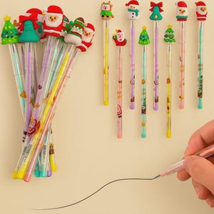 Pode incluir: Uma coleção de canetas de gel coloridas com tema natalino. As canetas apresentam vários enfeites festivos, incluindo Papai Noel, bonecos de neve e árvores de Natal. As canetas estão em tubos de plástico transparente, e uma mão desenha uma linha com uma caneta rosa.