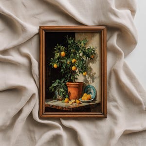 Op de afbeelding: Een ingelijst stilleven schilderij met een pot sinaasappelboom vol rijpe sinaasappels. Het schilderij bevat een klein blauw-wit bord met sinaasappels en een terracotta pot. Het kunstwerk is geplaatst tegen een neutrale achtergrond.