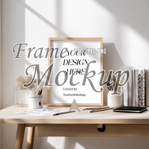 Könnte beinhalten: Ein Holzrahmen-Mockup mit dem Text "Frame Your Design Here Mockup" auf einem hellen Holzschreibtisch. Der Schreibtisch hat eine kleine Schublade, Bleistifte, ein Notizbuch und eine Vase mit Pinseln und Trockenblumen.