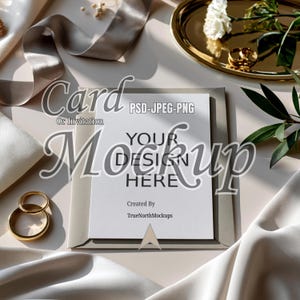 May include: A mockup card or invitation with the text "Your Design Here" is displayed on a neutral background. The card is surrounded by satin fabric, a gold tray with a flower, and gold rings. The text "Card Or Invitation" is also visible.