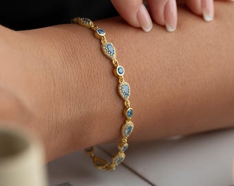 May include: A gold bracelet featuring alternating blue teardrop and round gemstones. The bracelet is embellished with small, clear accent stones. The jewellery is displayed on a person's wrist.
