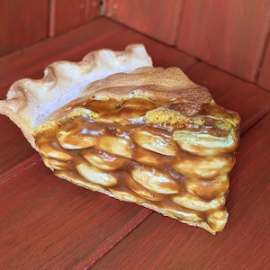May include: A ceramic slice of pie featuring a golden-brown, lattice-patterned crust filled with a glossy, amber-colored fruit filling. The top edge of the crust is crimped and textured, showing a realistic baked appearance with light and dark brown tones.