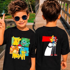May include: Black t-shirt with cartoon characters and the name "NOAH" in yellow. The back of the shirt has a graphic of a character with a red and white design. The shirt is worn by a person with sunglasses.