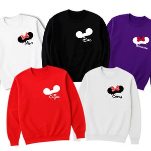 May include: Five crewneck sweatshirts in white, black, red, purple, and white. Each sweatshirt features a cartoon mouse ear design with a bow or text. The text includes "Mom", "Dad", "Elijah", "Emma", and "Grandma".