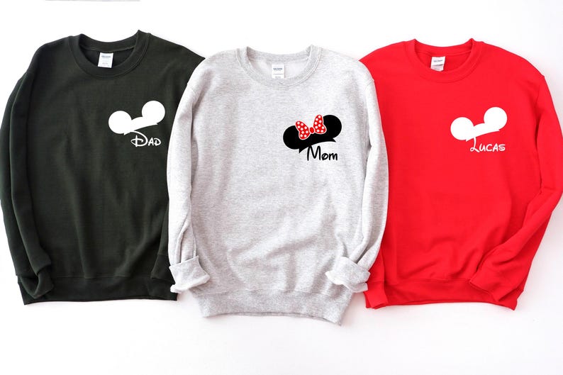 May include: Three sweatshirts in black, gray, and red. Each sweatshirt features a white Mickey Mouse head design. The black sweatshirt says "Dad", the gray sweatshirt has a Minnie Mouse bow and says "Mom", and the red sweatshirt says "Lucas".