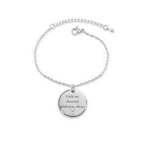 May include: A silver-colored bracelet with a delicate chain and a round pendant. The pendant is engraved with the words "Little me deserved gentleness, always" and a small teddy bear illustration. The bracelet is designed for everyday wear.