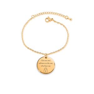 Può includere: Bracciale color oro con un ciondolo rotondo. Il ciondolo presenta l'incisione "I do not owe softness to the one who hurt me" e un simbolo di lucchetto. Il bracciale è su sfondo bianco.