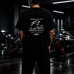 以下が含まれることがあります： 背面に白いグラフィックがプリントされた黒の半袖Tシャツ。ADDICTED TO F1の文字、レーシングカーの線画、SPEED IS A LIFESTYLEの文字、そして2本のチェッカーフラッグがデザインされています。