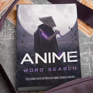 May include: A paperback book titled "ANIME WORD SEARCH" with a full moon and a silhouetted figure with a sword on the cover. The text reads "FEATURING OVER 80 POPULAR ANIME SHOWS & MOVIES". The book is on a patterned surface.