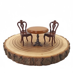 Op de afbeelding: Miniatuur bruine tafel en stoelen set. De ronde tafel heeft een donkerbruin blad en een sierlijke, donkere metalen voet. Twee bijpassende stoelen met decoratieve rugleuningen staan aan weerszijden van de tafel. De set wordt gepresenteerd op een houten schijf.
