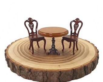 May include: Miniature brown table and chairs set. The round table has a dark brown top and ornate, dark metal base. Two matching chairs with decorative backs are on either side of the table. The set is displayed on a wooden slice.