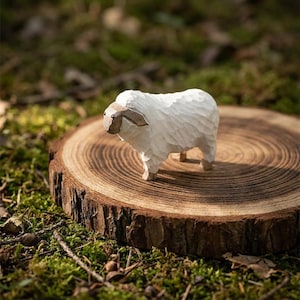 May include: A hand-carved wooden sheep figurine with a textured white body and brown ears and face. The sheep stands on a round, wooden tree stump, surrounded by green moss and leaves. The figurine is a charming decorative item.