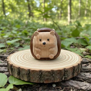May include: A wooden hedgehog figurine with a light brown body and a dark brown back. The hedgehog is carved with detailed features and sits on a small, round wooden slice. The background is a blurred forest scene.