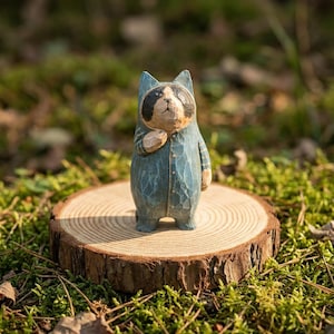 May include: A hand-carved wooden figurine of a raccoon wearing a blue jumpsuit, standing on a small wooden slice. The raccoon has a black mask and a light brown face. The figurine is set against a backdrop of green moss and foliage.