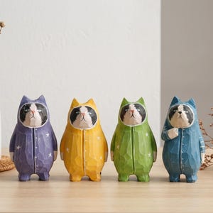May include: Four carved wooden cat figurines in pajamas. The cats are painted in purple, yellow, green, and blue, each with a different color of star accents. The cats have black and white faces and are standing upright.