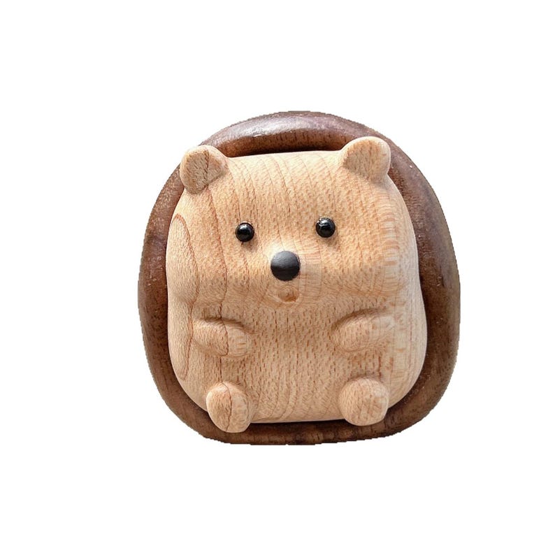 May include: A wooden hedgehog figurine with a light brown body and a dark brown, oval-shaped back. The hedgehog has small, black eyes and a black nose. The figurine is carved with visible wood grain and has a smooth finish.