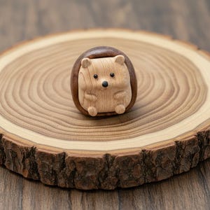 May include: A handcrafted wooden hedgehog figurine with a light brown body and a dark brown back. The hedgehog has small black eyes and a black nose. The figurine is set on a round wooden slice with visible growth rings.