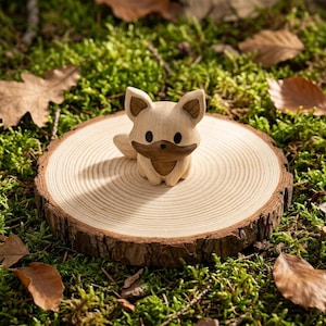 K&ouml;nnte beinhalten: Eine kleine, geschnitzte Holzfigur eines Fuchses mit hellbraunem K&ouml;rper und einem dunkelbraunen Fleck &uuml;ber Gesicht und Ohren. Der Fuchs hat zwei schwarze, runde Augen und eine kleine schwarze Nase und sitzt auf einer hellen Holzscheibe.