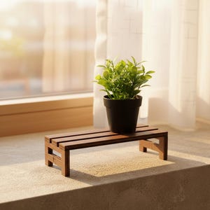 Peut inclure: Un petit support de plante en bois brun foncé avec une plante en pot noire. La plante a des feuilles vertes. Le support est rectangulaire avec trois lattes horizontales et est placé sur un rebord de fenêtre.