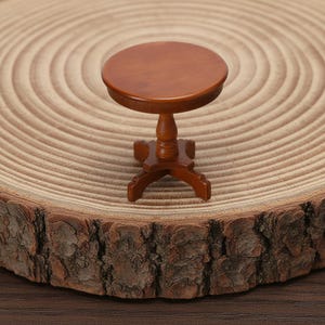 Könnte beinhalten: Ein Miniatur-Holztisch mit runder Tischplatte und einem Sockel. Der Tisch ist in einem satten Braunton gehalten und scheint aus poliertem Holz zu bestehen. Der Tisch ist etwa 7.6 cm hoch.