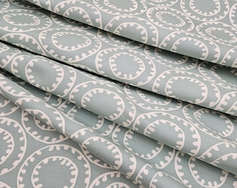May include: A light sage green fabric featuring a repeating pattern of white circular motifs. Each circle is outlined with a thick border and contains a series of small, evenly spaced white dashes along the inner edge, creating a consistent geometric design.