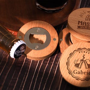 May include: Wooden bottle openers and coasters. The bottle opener has a stainless steel opener in the center, surrounded by a wooden frame. The coasters are round, wooden, and engraved with names and dates. A beer bottle is in the image.
