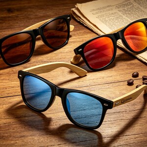 Pu&ograve; includere: Tre paia di occhiali da sole con montatura nera e aste in legno sono esposti su una superficie di legno. Le lenti sono marroni, rosse e blu. Chicchi di caff&egrave; e un giornale sullo sfondo.
