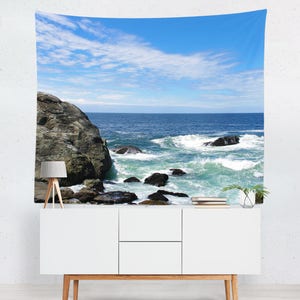 May include: A tapestry featuring a scenic ocean view with a rocky shoreline and crashing waves. The sky is a bright blue with white clouds.