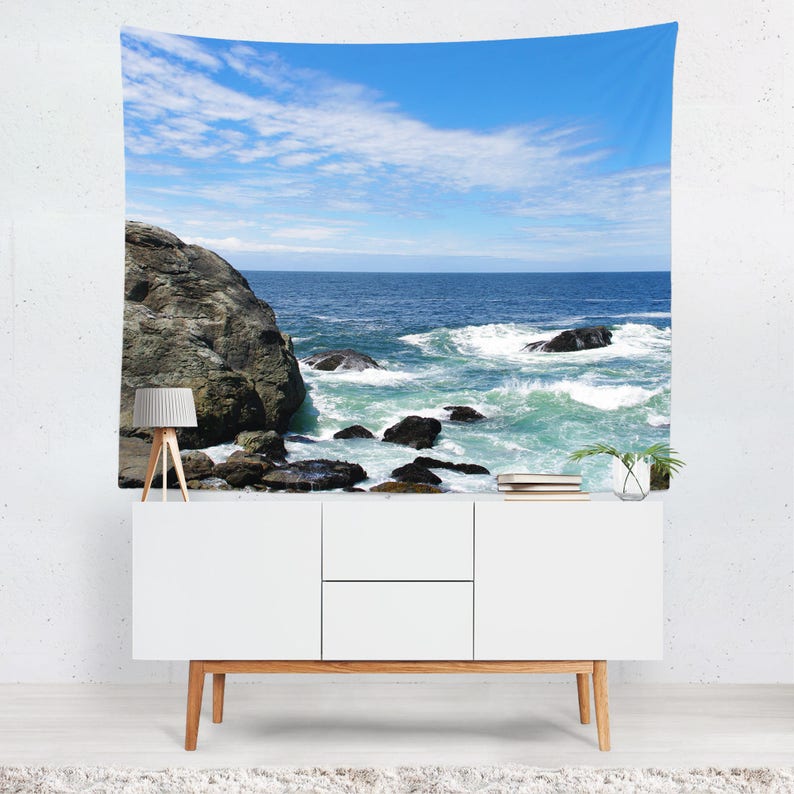 May include: A tapestry featuring a scenic ocean view with a rocky shoreline and crashing waves. The sky is a bright blue with white clouds.