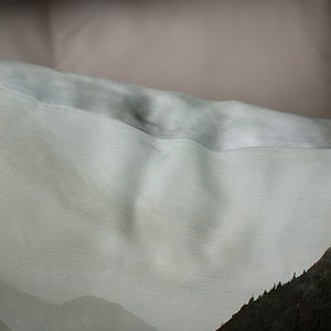 May include: A light green and gray fabric with a subtle texture. The fabric has a mountain scene printed on it.