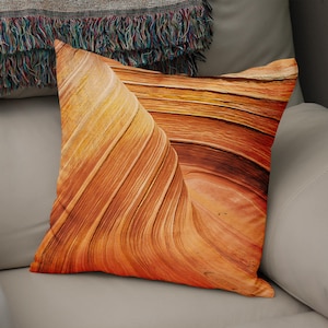 May include: A close-up of a pillow featuring a photograph of a sandstone formation with a swirling, layered pattern in shades of orange, brown, and yellow.