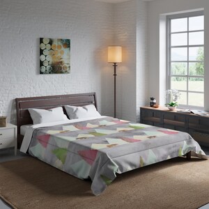 May include: A grey comforter featuring a repeating pattern of light green and pink triangles, interspersed with small brown bear silhouettes. The bedding is draped over a bed frame with two white pillows positioned at the head of the mattress.