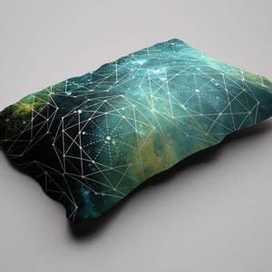 Op de afbeelding: Een teal en groen kussen met een geometrisch patroon van witte lijnen en stippen. Het patroon lijkt op een sterrenbeeld of galaxie.