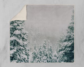 May include: A snowy winter scene with a forest of evergreen trees covered in white snow. The trees are silhouetted against a hazy, grey sky.