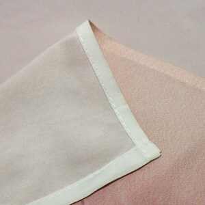 May include: Close-up of a white fabric seam with a light pink fabric underneath. The seam is stitched with a straight stitch.