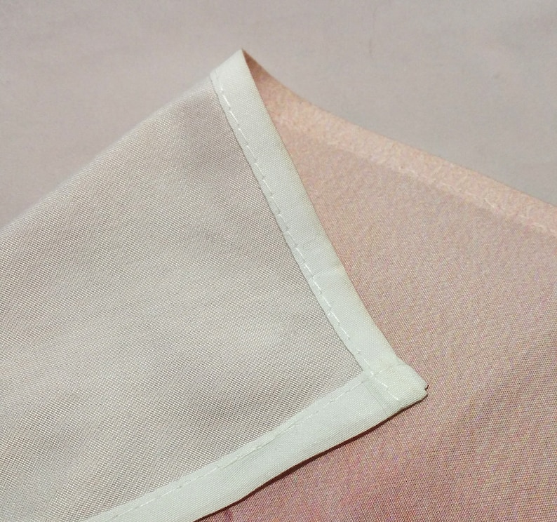 May include: Close-up of a white fabric seam with a light pink fabric underneath. The seam is stitched with a straight stitch.