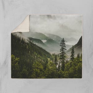 May include: A misty mountain landscape with a valley filled with lush green trees. The fog creates a sense of mystery and serenity.
