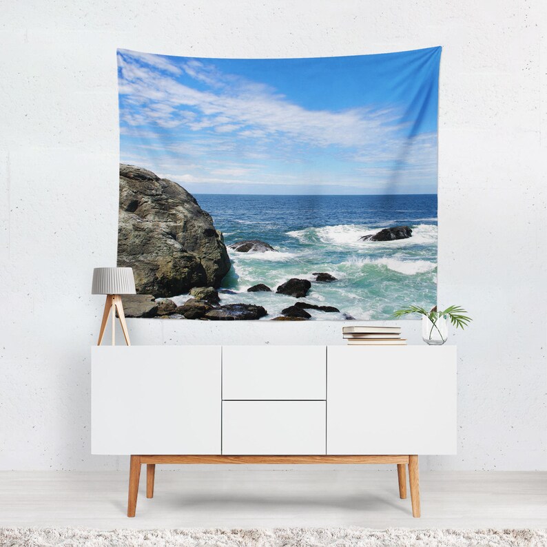 May include: A tapestry featuring a scenic ocean view with a rocky shoreline and crashing waves. The sky is a bright blue with white clouds.