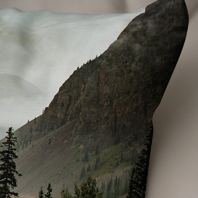 May include: A close-up of a mountainside with a rocky, green, and brown texture. The mountain is covered in a light mist, and there are trees growing on the slopes.